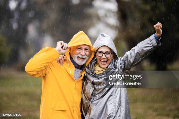 couple d’âge mûr heureux en imperméable s’amusant pendant la pluie dans le parc. - kway photos et images de collection