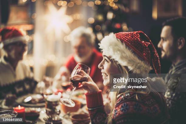 happy woman with santa's drinking wine during christmas lunch at dining table. - santa hat imagens e fotografias de stock