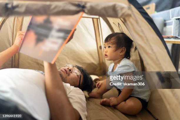 close up facial expression daughter lying down and enjoying reading a picture book with her father inside the small tent for baby at living room domestic life. - book close up stock-fotos und bilder