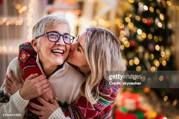 cariñosa hija adulta besando a su madre madura el día de navidad en casa. - friends kissing cheeks fotografías e imágenes de stock