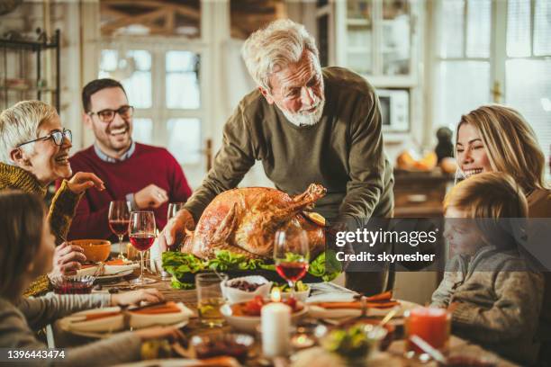 happy senior man serving thanksgiving turkey for his family at dining table. - happy thanksgiving stockfoto's en -beelden