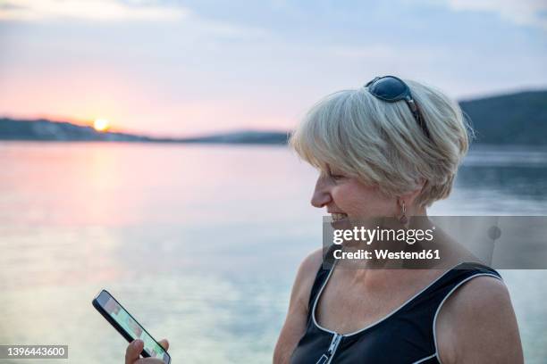 smiling senior woman doing video call through smart phone by sea on sunset - old woman short hair stock pictures, royalty-free photos & images