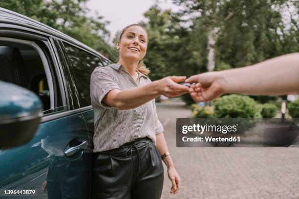 smiling woman giving car key to man at parking lot - car keys hand stockfoto's en -beelden