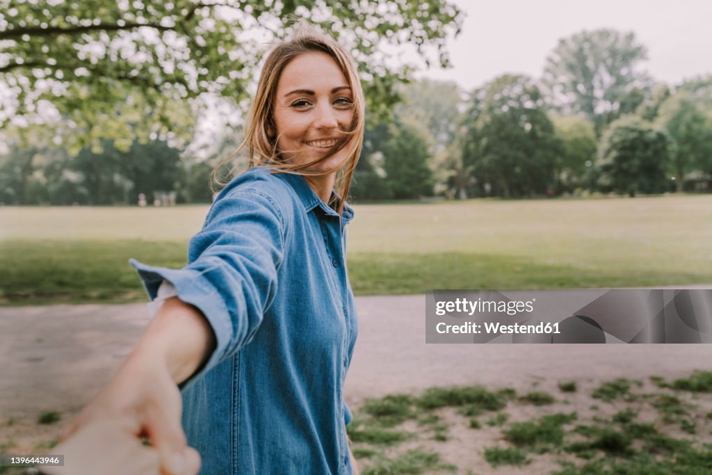 Smiling young woman pulling friend's hand in park