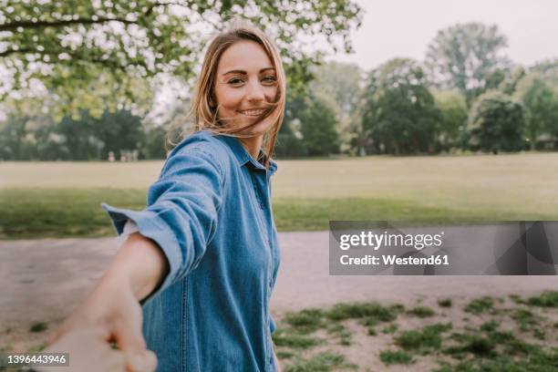 smiling young woman pulling friend's hand in park - pulling stock pictures, royalty-free photos & images