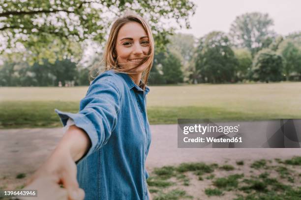 smiling young woman pulling friend's hand in park - röra mot bildbanksfoton och bilder