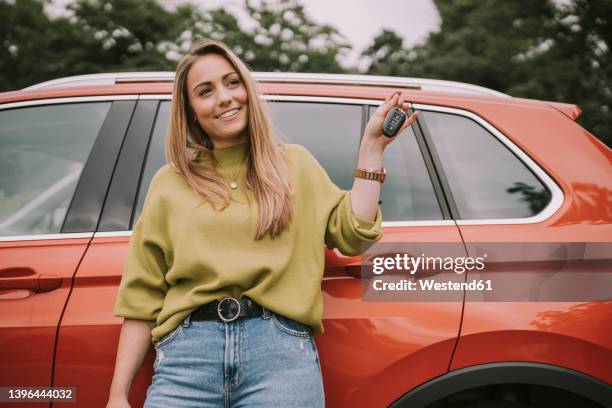 smiling young woman with key standing in front of car - car keys stock pictures, royalty-free photos & images