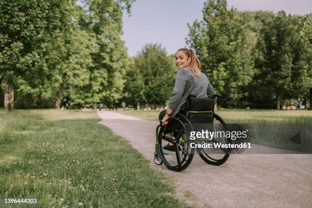 young woman sitting in wheelchair at park - wheelchair stock pictures, royalty-free photos & images
