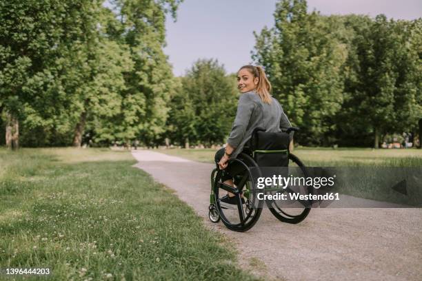 young woman sitting in wheelchair at park - wheel chair stock pictures, royalty-free photos & images