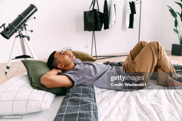 thoughtful man with hands behind head lying on bedding at home - materasso foto e immagini stock
