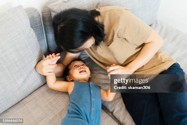 positive emotion asian mother with baby girl daughter playing seeks and hide on sofa domestic life at home. - pursuit stock pictures, royalty-free photos & images