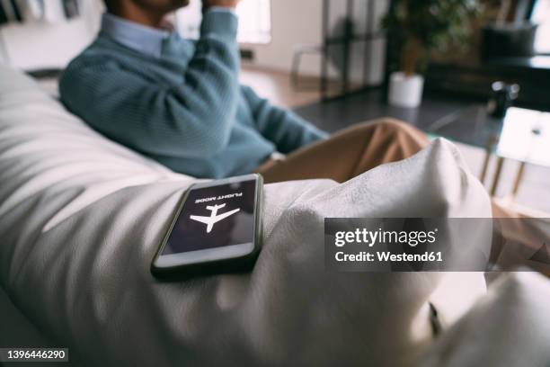 flight mode symbol on mobile phone by man sitting on sofa at home - mobile worker stockfoto's en -beelden