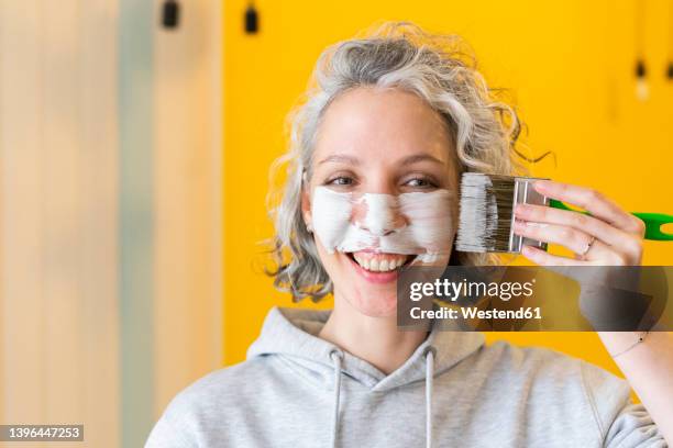 smiling playful woman applying white paint on face with paintbrush - adult interior home stock pictures, royalty-free photos & images