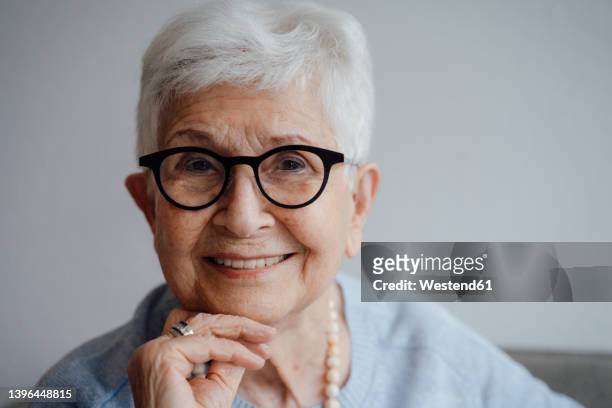 happy senior woman with hand on chin at home - aging happy stockfoto's en -beelden