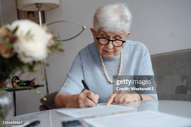 senior woman writing on paper sitting at home - testamento imagens e fotografias de stock