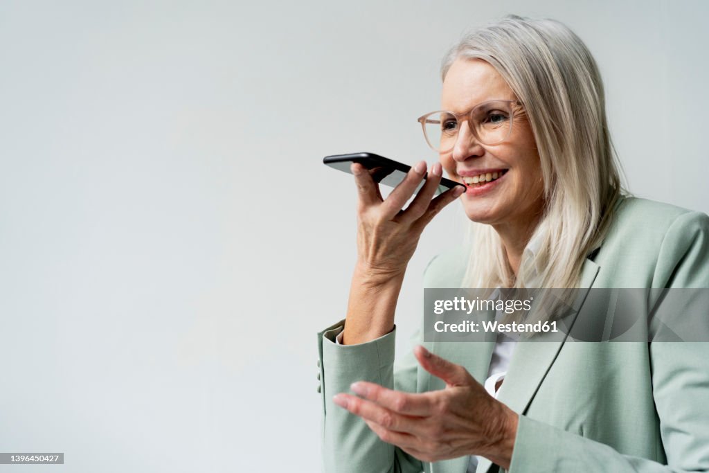 Businesswoman talking on speaker phone against white background