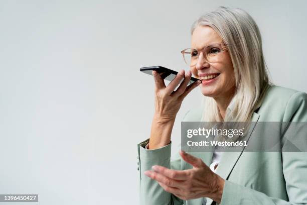 businesswoman talking on speaker phone against white background - conference phone stock pictures, royalty-free photos & images