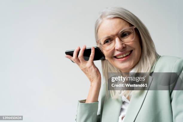 smiling businesswoman listening voice through phone speaker against white background - conference phone stock pictures, royalty-free photos & images