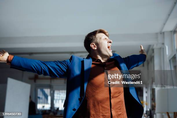 businessman with arms outstretched yawning in office - yawn office stockfoto's en -beelden