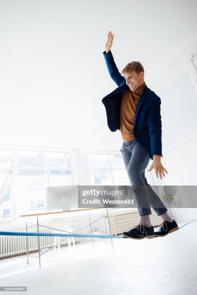 Businessman with hand raised balancing on tightrope in office