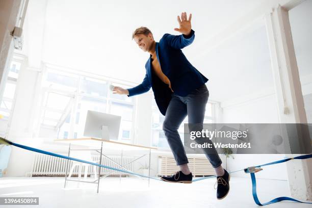 happy businessman balancing on tightrope in office - slacklining stock-fotos und bilder