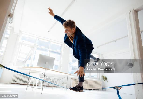 happy businessman slacklining in office - slackline stock-fotos und bilder