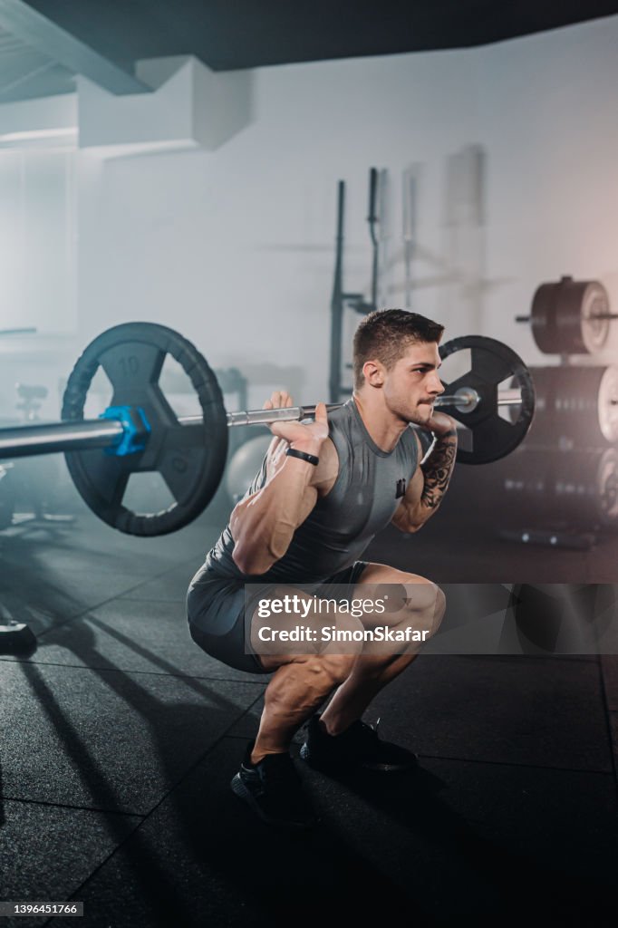 Determined male athlete exercising with barbell during weight training in gym