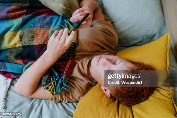 teenage boy using smart phone lying on bed in bedroom - boys relaxing stock-fotos und bilder