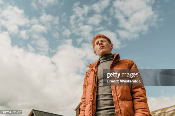 contemplative teenage boy standing under cloudy sky - redhead teen fotografías e imágenes de stock