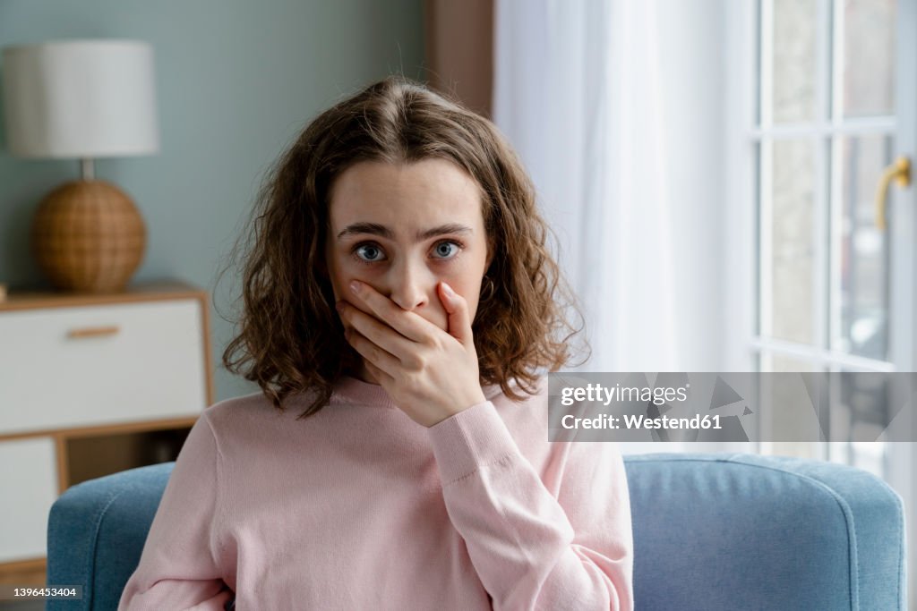 Young woman covering mouth with hand at home