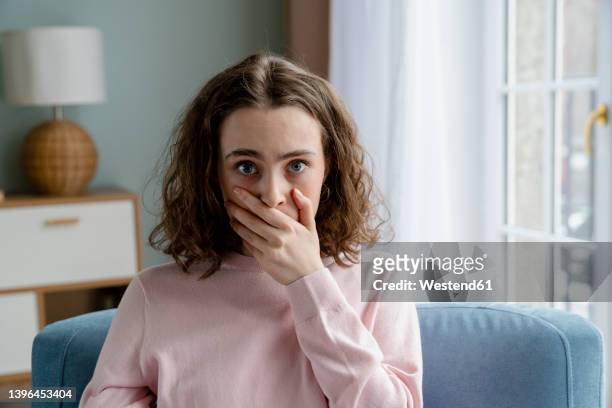 young woman covering mouth with hand at home - hands covering mouth stock pictures, royalty-free photos & images