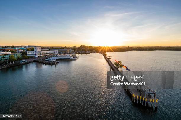 germany, baden-wurttemberg, friedrichshafen, aerial view of town on shore of lake constance at sunrise with long pier in foreground - bodensee stock pictures, royalty-free photos & images