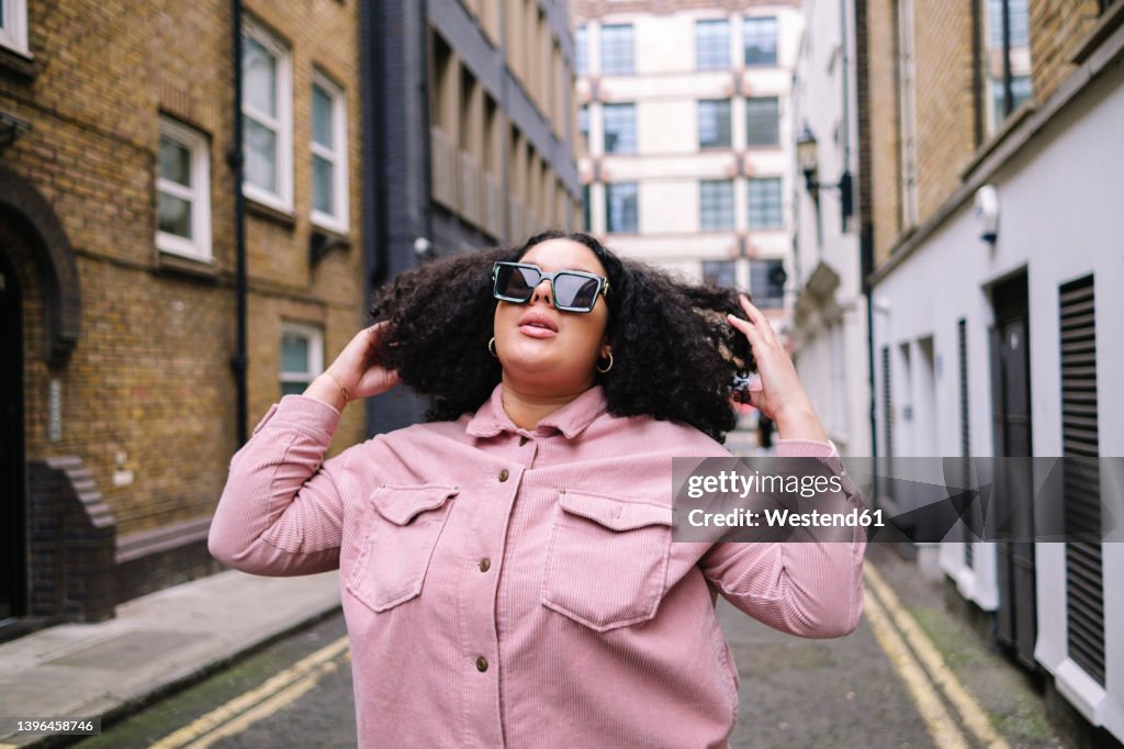 Young woman wearing sunglasses standing with hand in hair