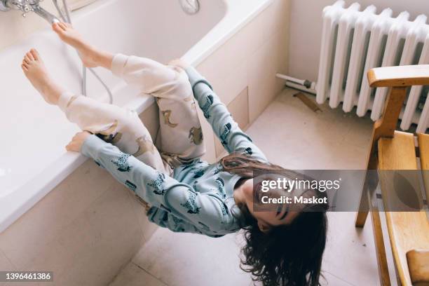 portrait of playful girl hanging on bathtub - heizung stock-fotos und bilder