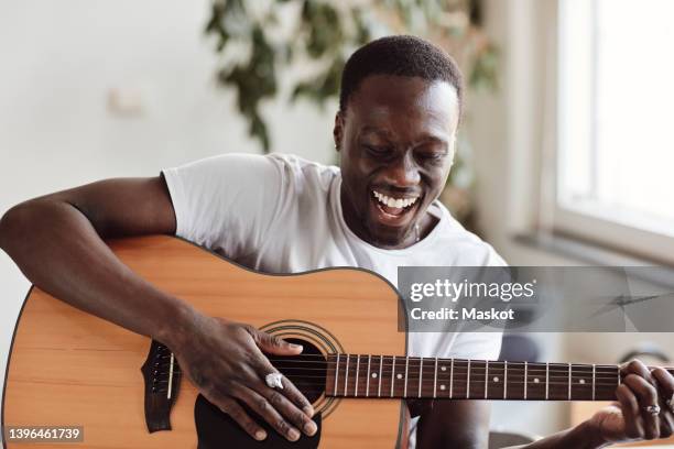 happy male artist singing while practicing guitar in classroom - instrumento de cuerdas fotografías e imágenes de stock