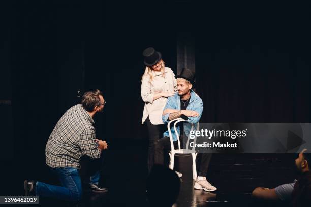 instructor looking at man and woman wearing hat rehearsing on stage - faire du théâtre photos et images de collection