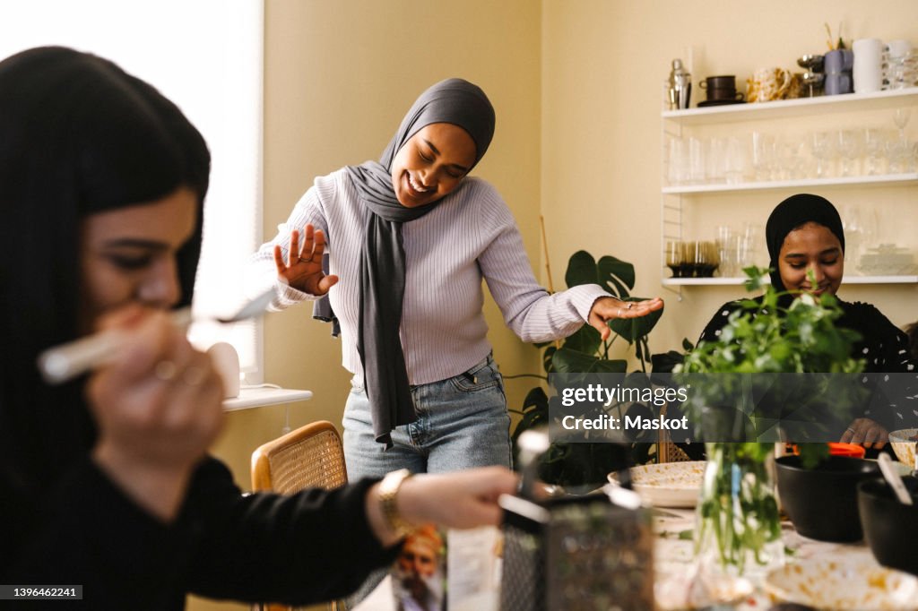 Happy young woman dancing while female friends preparing food at table in kitchen