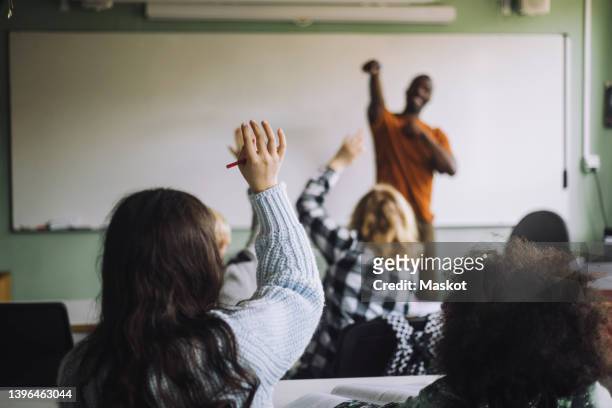 rear view of girl raising hand while sitting with students in classroom - sweden school stock pictures, royalty-free photos & images