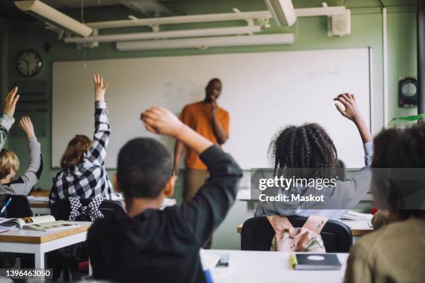 rear view of multiracial students raising hands in classroom during lecture - sweden school stock pictures, royalty-free photos & images