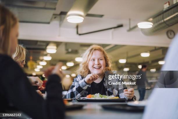 smiling boy taking with friends during lunch break in cafeteria at school - lunchpauze stockfoto's en -beelden