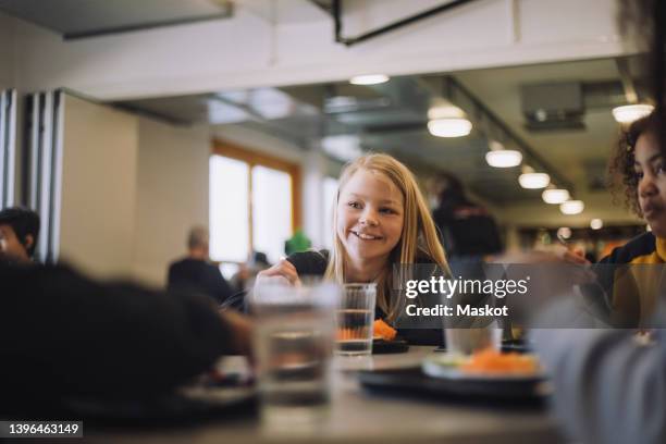 smiling girl enjoying food with friends during lunch break at school - schulessen stock-fotos und bilder