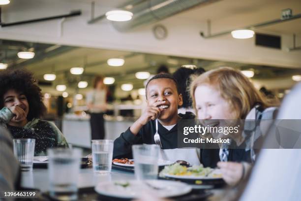 friends laughing while having food at table during lunch break in cafeteria - cantina imagens e fotografias de stock