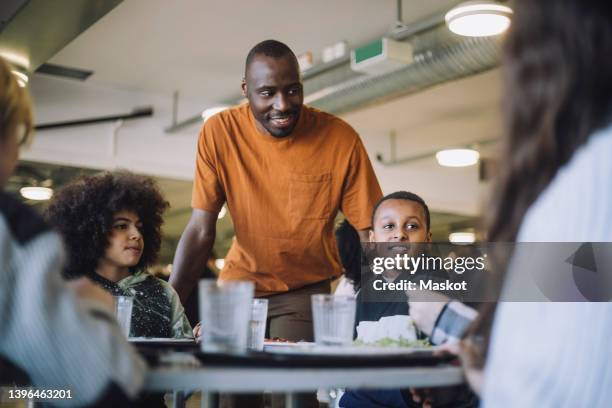 smiling teacher standing by students during lunch break in cafeteria - middle school lunch stock pictures, royalty-free photos & images