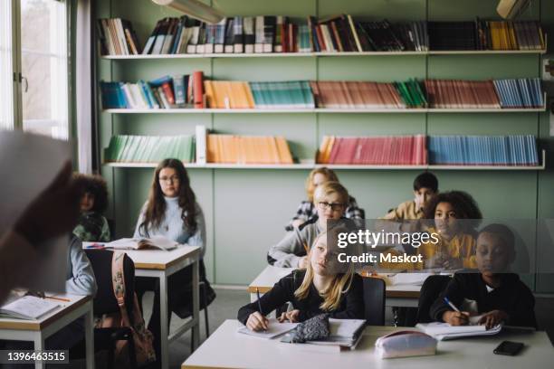 diverse students writing while listening to teacher during lecture in classroom - school scandinavia stock pictures, royalty-free photos & images