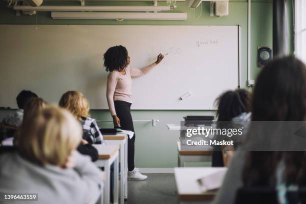 side view of teacher explaining mathematics to students on white board in classroom - teachers imagens e fotografias de stock