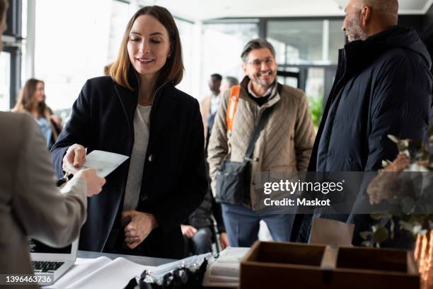 businesswoman taking id card from receptionist at registering counter in convention center - iscrizione nelle liste elettorali foto e immagini stock