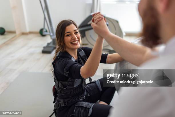 caucasian female client in ems suit interchange high five with instructor - electrode stock pictures, royalty-free photos & images