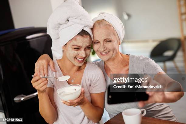 mujeres sonrientes con máscaras faciales al hablar selfie en casa - mother daughter towel fotografías e imágenes de stock