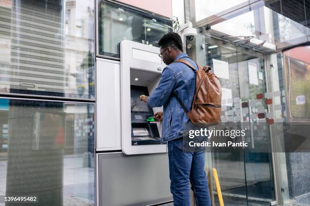 young man retrieving money from his bank account - geldautomaat stockfoto's en -beelden