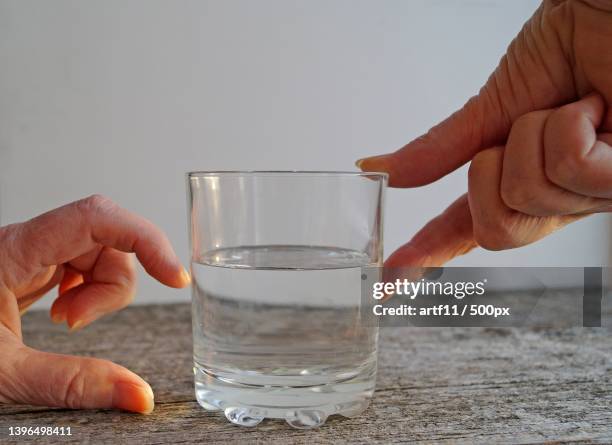 cropped hand of people comparing glass half full or empty over white background - glass of water hand ストックフォトと画像